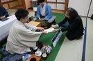 立会人の福崎文吾九段（右）に封じ手を手渡す菅井竜也八段。奥は藤井聡太王将‖大田市三瓶町、国民宿舎さんべ荘（提供：日本将棋連盟）