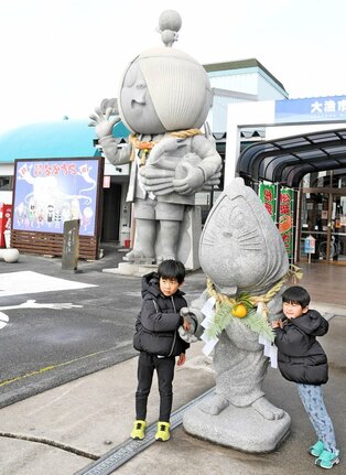 しめ縄が飾られた石像との記念撮影を楽しむ子どもたち＝境港市竹内団地、大漁市場なかうら