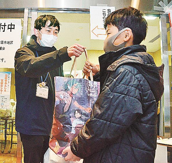 新聞紙で作った紙袋に入ったお菓子を受け取る子ども＝出雲市今市町、出雲市社会福祉センター