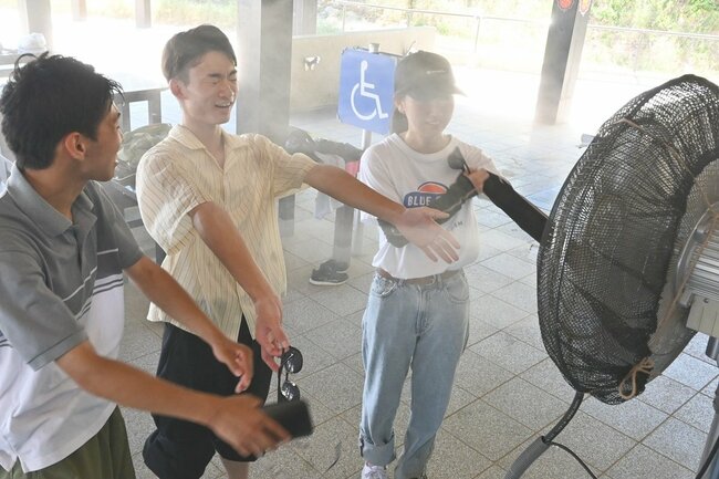 日陰に設置された水蒸気の出る扇風機で涼む人たち＝鳥取市福部町湯山、鳥取砂丘ビジターセンター