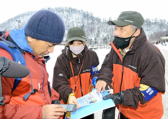 登山者(左)にスマートフォンを使った登山届の提出方法を伝える警察官=鳥取県大山町大山