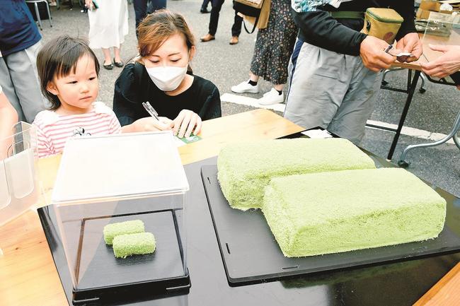 巨大な若草の重さを推測する親子連れ。左は通常サイズの若草＝松江市八束町波入、彩雲堂八束工場