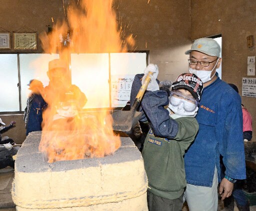 たたら製鉄の技術者に見守られ、炉に砂鉄を入れる児童＝島根県奥出雲町大呂、鳥上小学校古代たたら体験学習工房