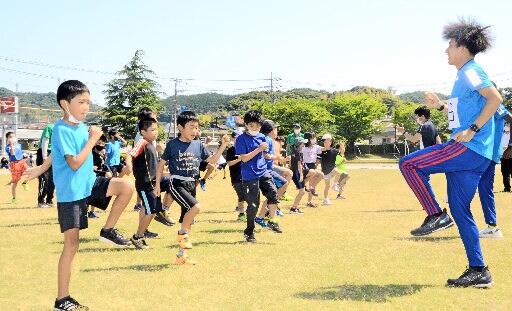 山口和也選手（右）の指導で、もも上げをする小学生＝浜田市黒川町、市陸上競技場