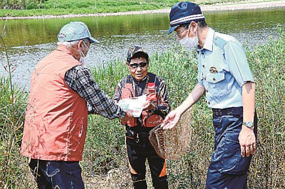 釣り人（中央）にチラシを渡してマナーアップの協力を呼びかける高津川漁業協同組合員と益田署員＝益田市横田町