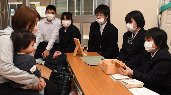 １歳児健診に訪れた親子に積み木を紹介し、贈呈する石見養護学校の生徒＝島根県邑南町淀原、町健康センター元気館
