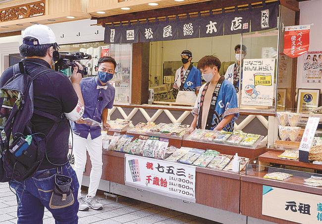 川崎大師の参道沿いで、あめ専門店を紹介する磯谷祥太さん（左から２人目）