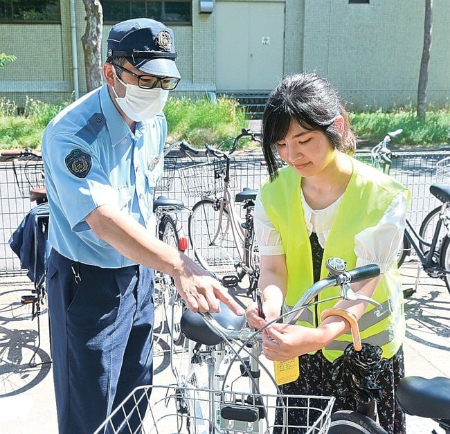 警察官に教わり自転車施錠の注意喚起をする学生＝松江市西川津町、島根大