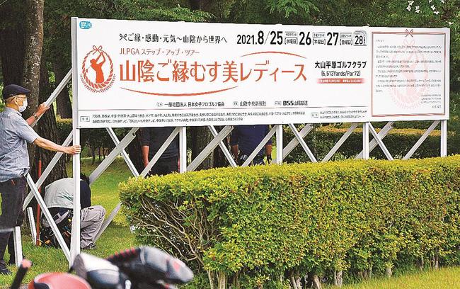 練習グリーン奥に「山陰ご縁むす美レディース」の開催をアピールする大型看板を設置する関係者＝鳥取県伯耆町丸山、大山平原ゴルフクラブ