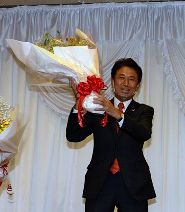 当選確実の報を受け、祝勝会会場で花束を手に喜ぶ飯塚俊之氏