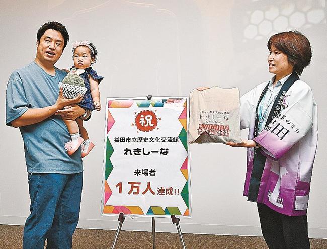 １万人目の来場者となり、記念品のアムスメロンを手にする中山純平さん（左）＝益田市本町、市立歴史文化交流館・れきしーな