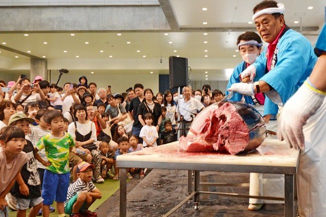 深町誠人さん（右）らによるクロマグロの解体ショーに見入る来場者たち＝境港市昭和町、県営境港水産物地方卸売市場２号上屋