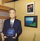 これまでのコンテスト入選作品と写真に収まる安達彰さん＝松江市浜乃木５丁目