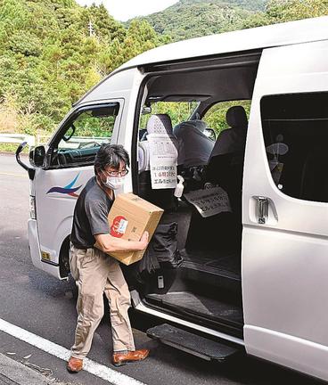 食料品の入った箱を抱えてシャトルバスを降りる日御碕地区の住民＝出雲市大社町日御碕