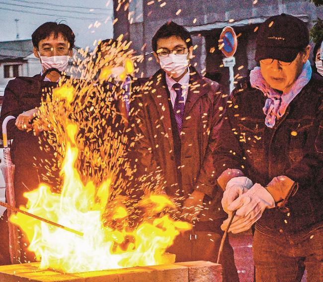 簡易式の炉に木炭を入れて燃やす関係者（右）＝松江市学園南１丁目、くにびきメッセ駐車場